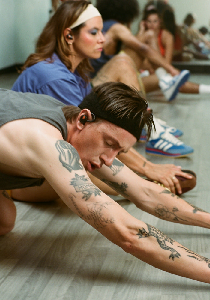 Man in a sweatband and tank top in a dusty gym while wearing Skullcandy earbuds with flexible ear hooks